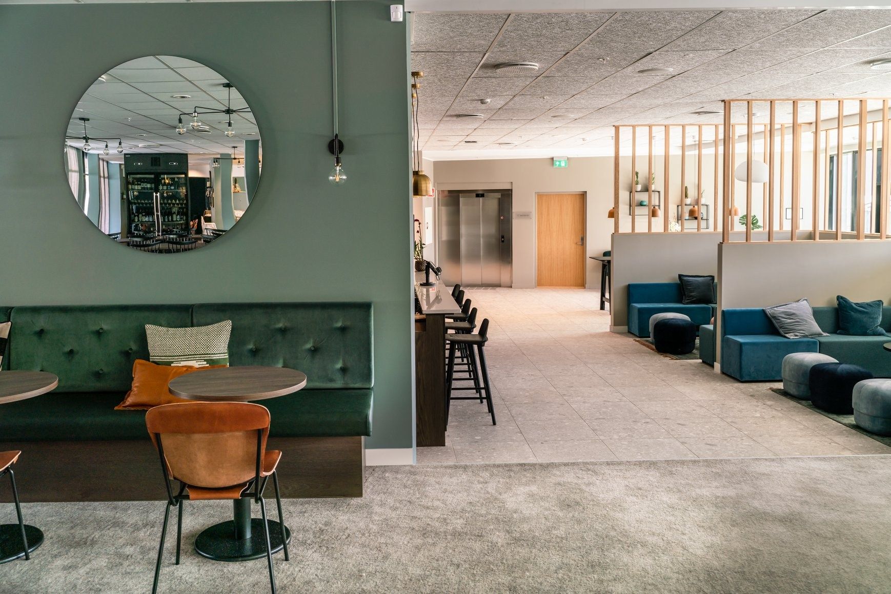 Moderne kaféområde med grøne møblar og ein rund spegel på veggen.