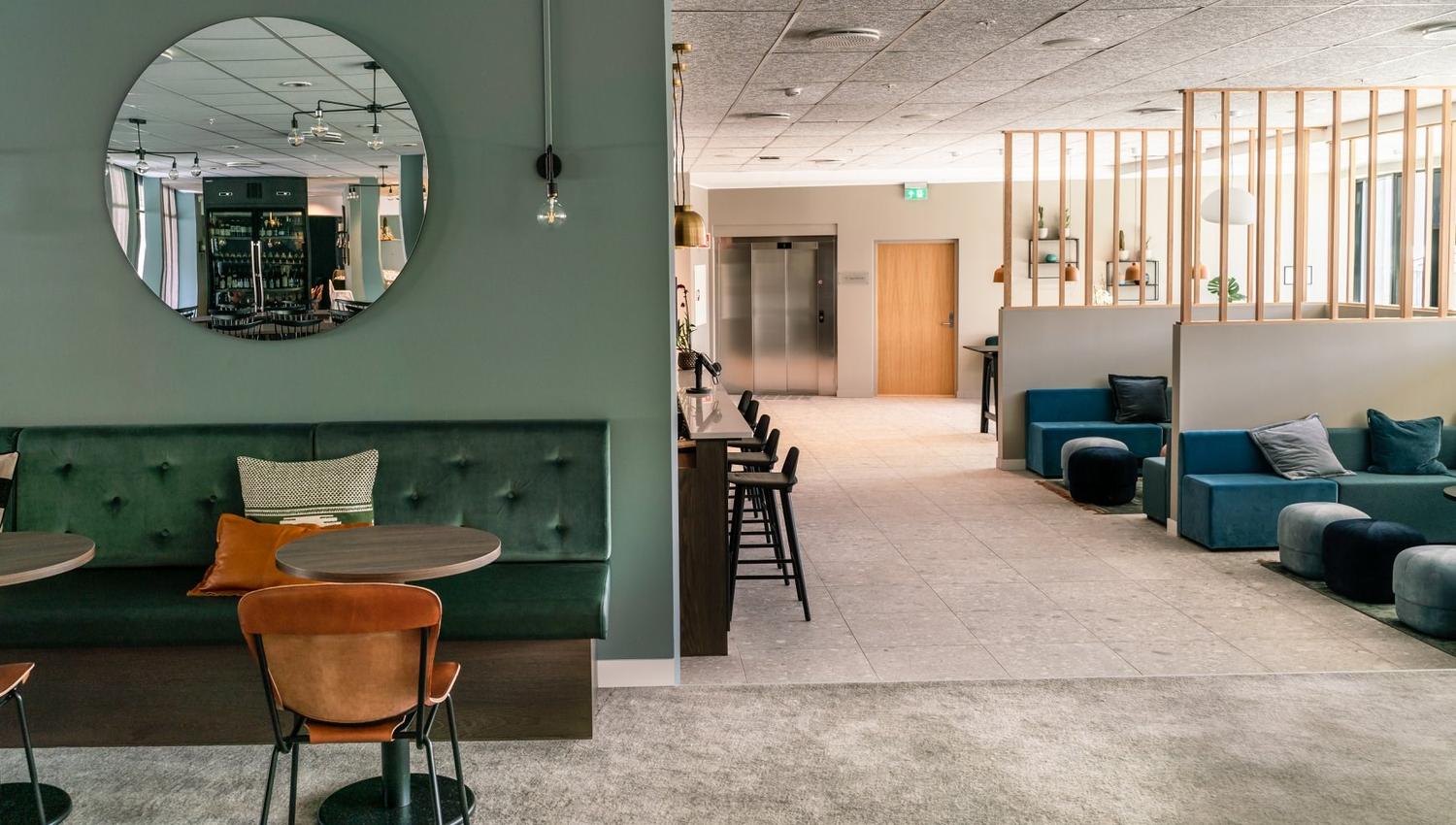Moderne kaféområde med grøne møblar og ein rund spegel på veggen.
