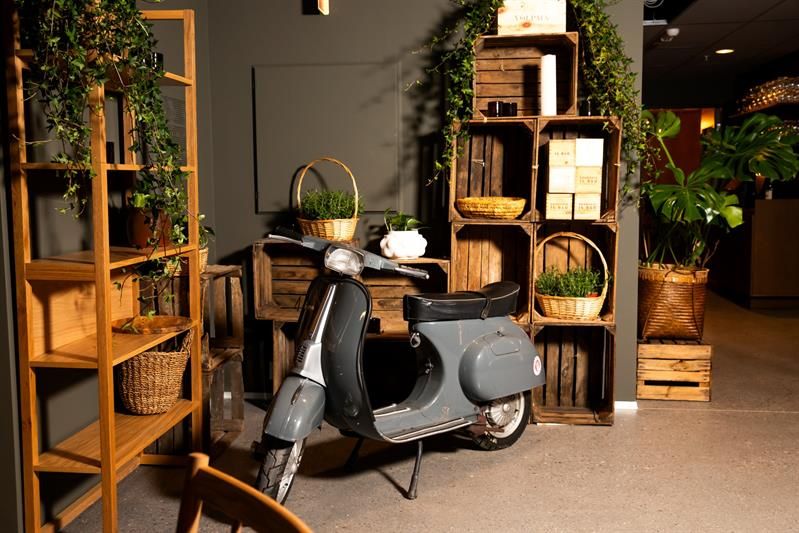 En moped som står inne i lokalet foran hyller og kurver med planter
