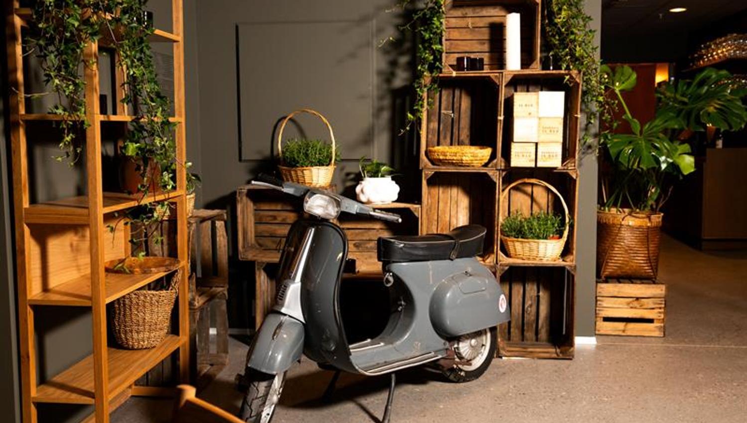 En moped som står inne i lokalet foran hyller og kurver med planter