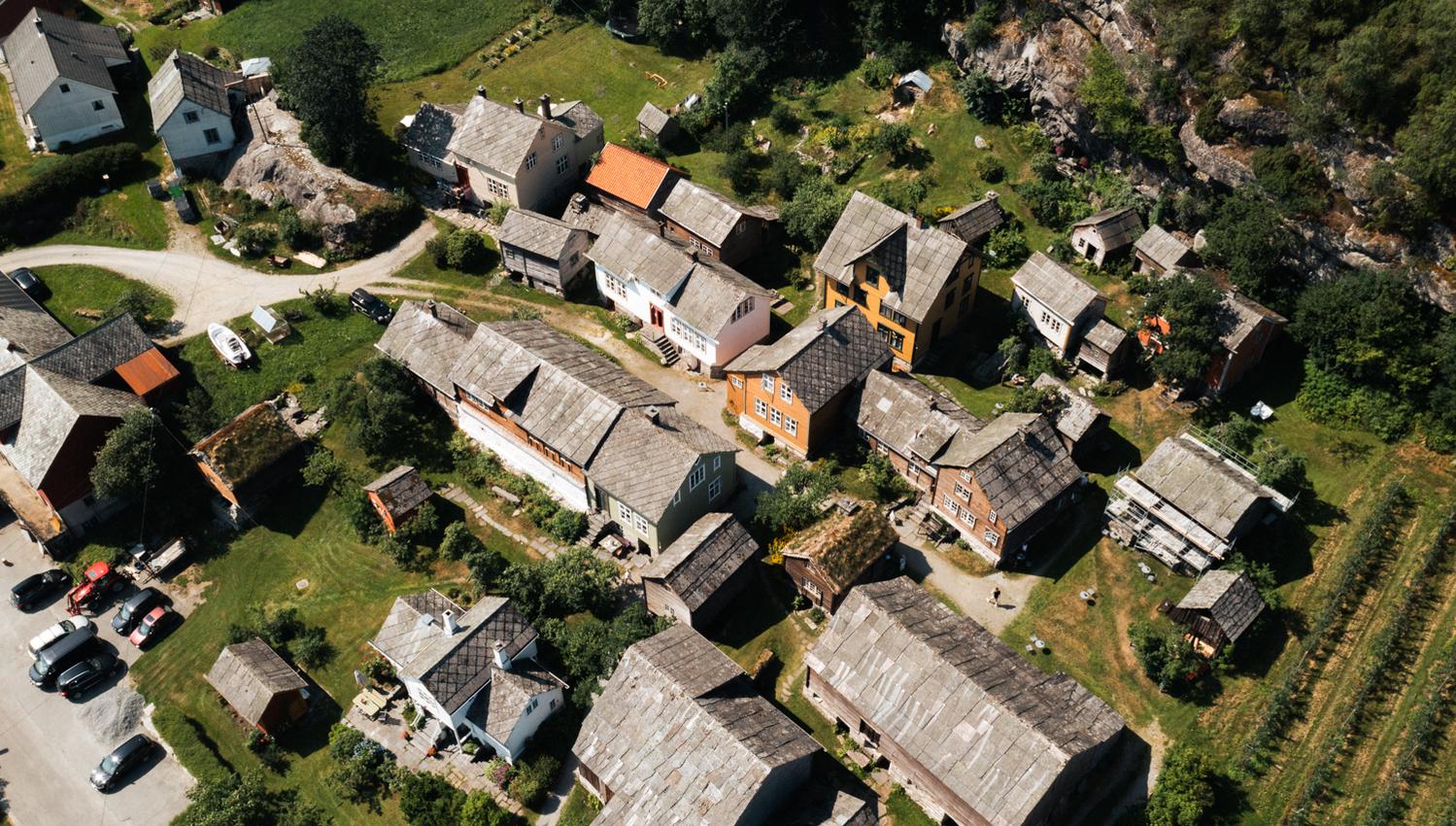 Dronefoto av Agatunet med historiske trehus tett samla, omgitt av grønt landskap og frukthager.