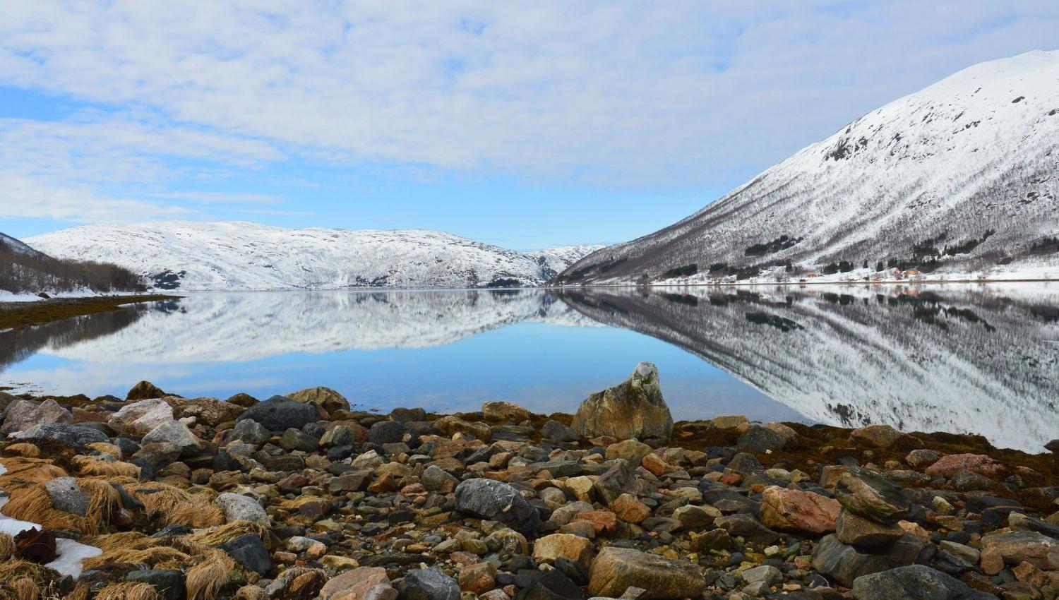 Fjære med klart hav og fjell i bakgrunnen