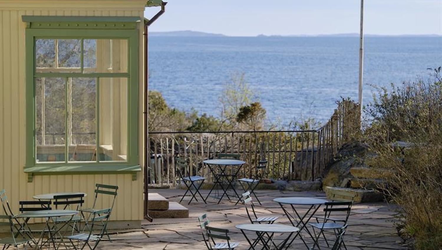 Table and chairs in front of a yellow house and the sea in the background