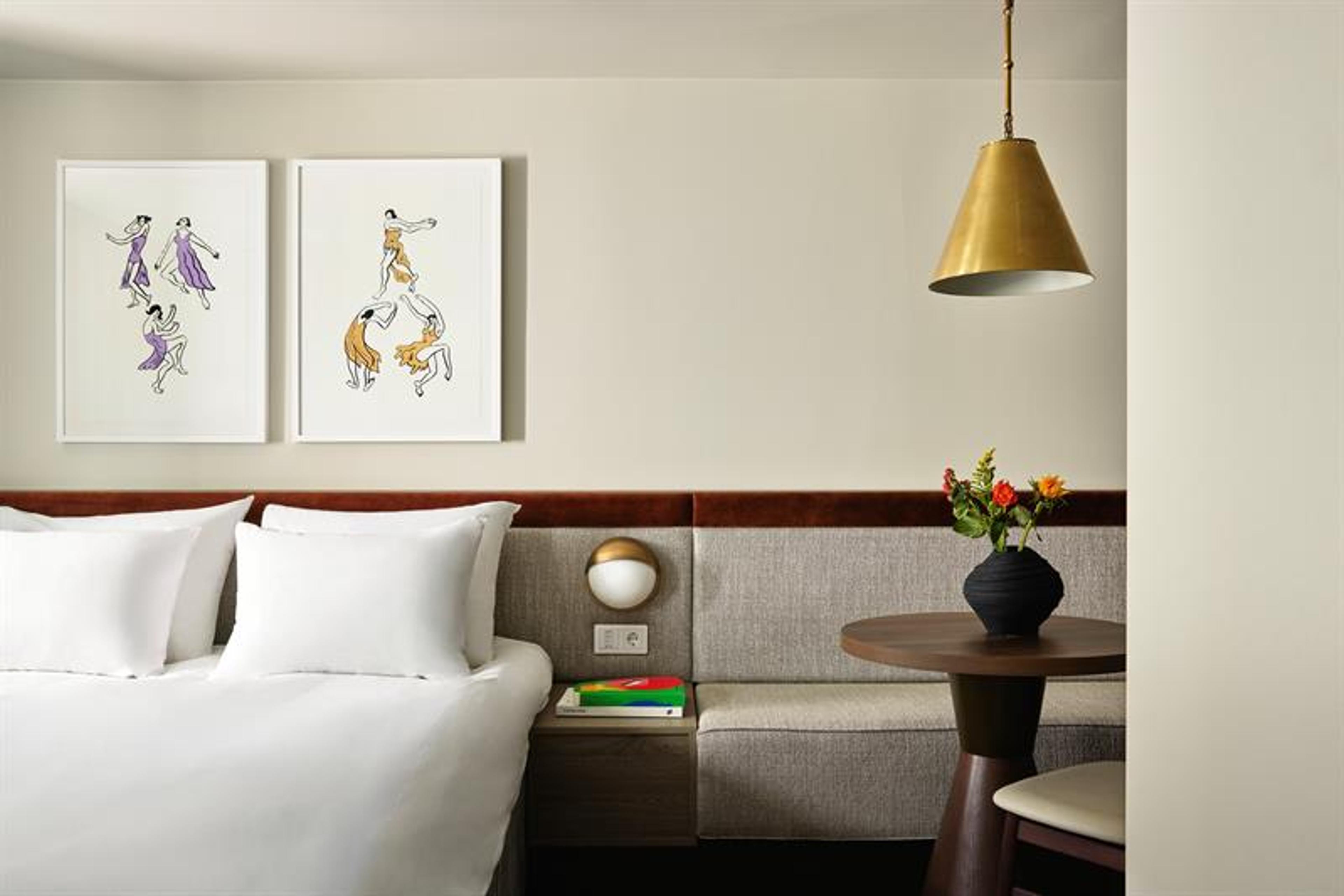 The rooms feature a double bed, integrated seating and wall-mounted lighting. The interior combines textiles, wood finishes and framed artwork.