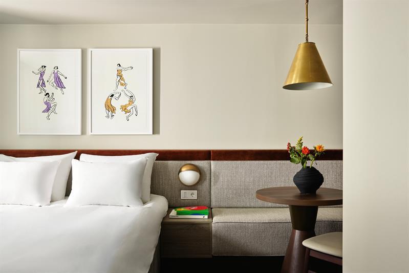 The rooms feature a double bed, integrated seating and wall-mounted lighting. The interior combines textiles, wood finishes and framed artwork.