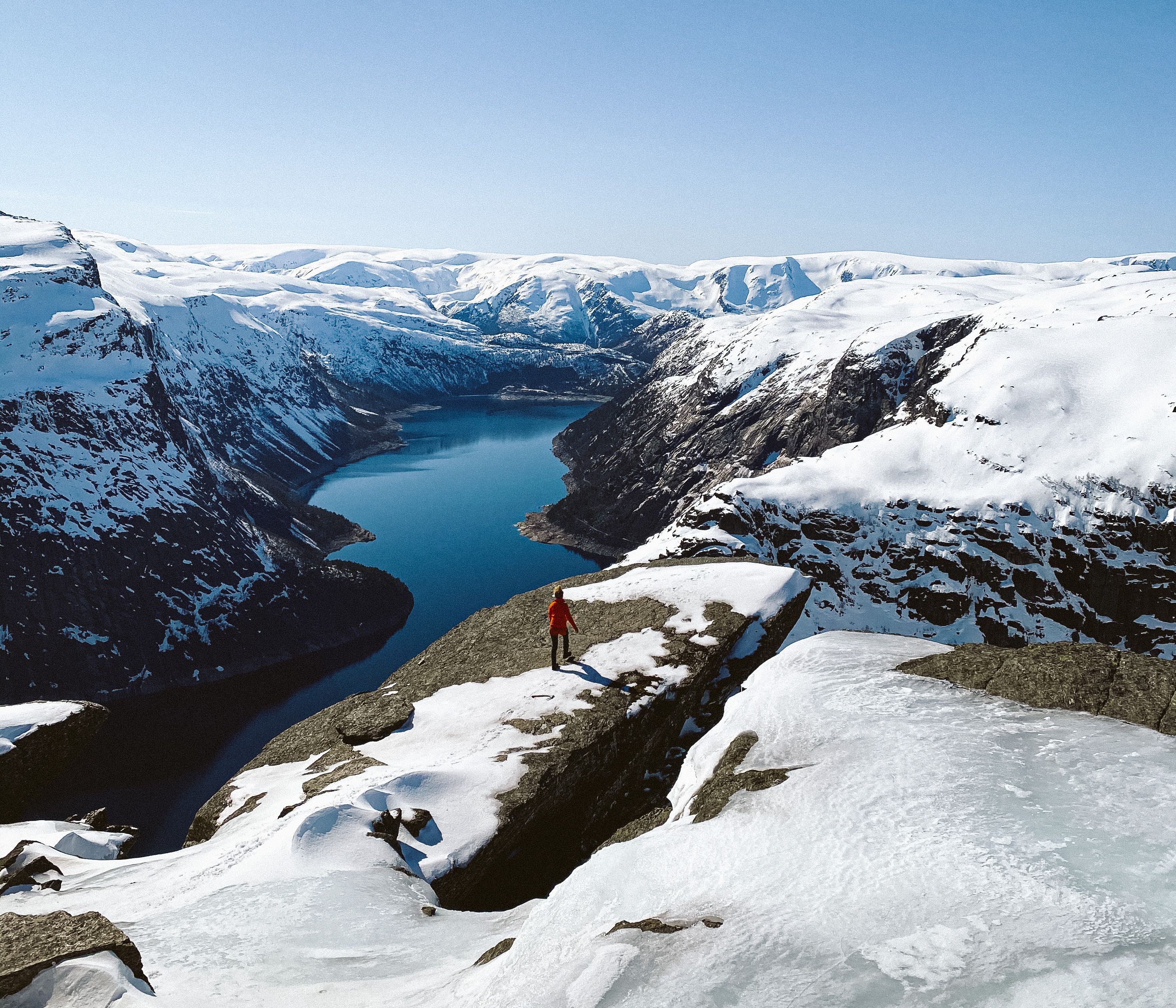 Hiker standing at the edge with panoramic views of the fjord and winter mountains at Trolltunga.