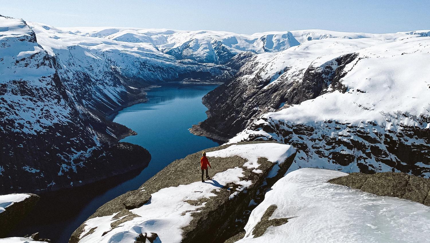 Hiker standing at the edge with panoramic views of the fjord and winter mountains at Trolltunga.