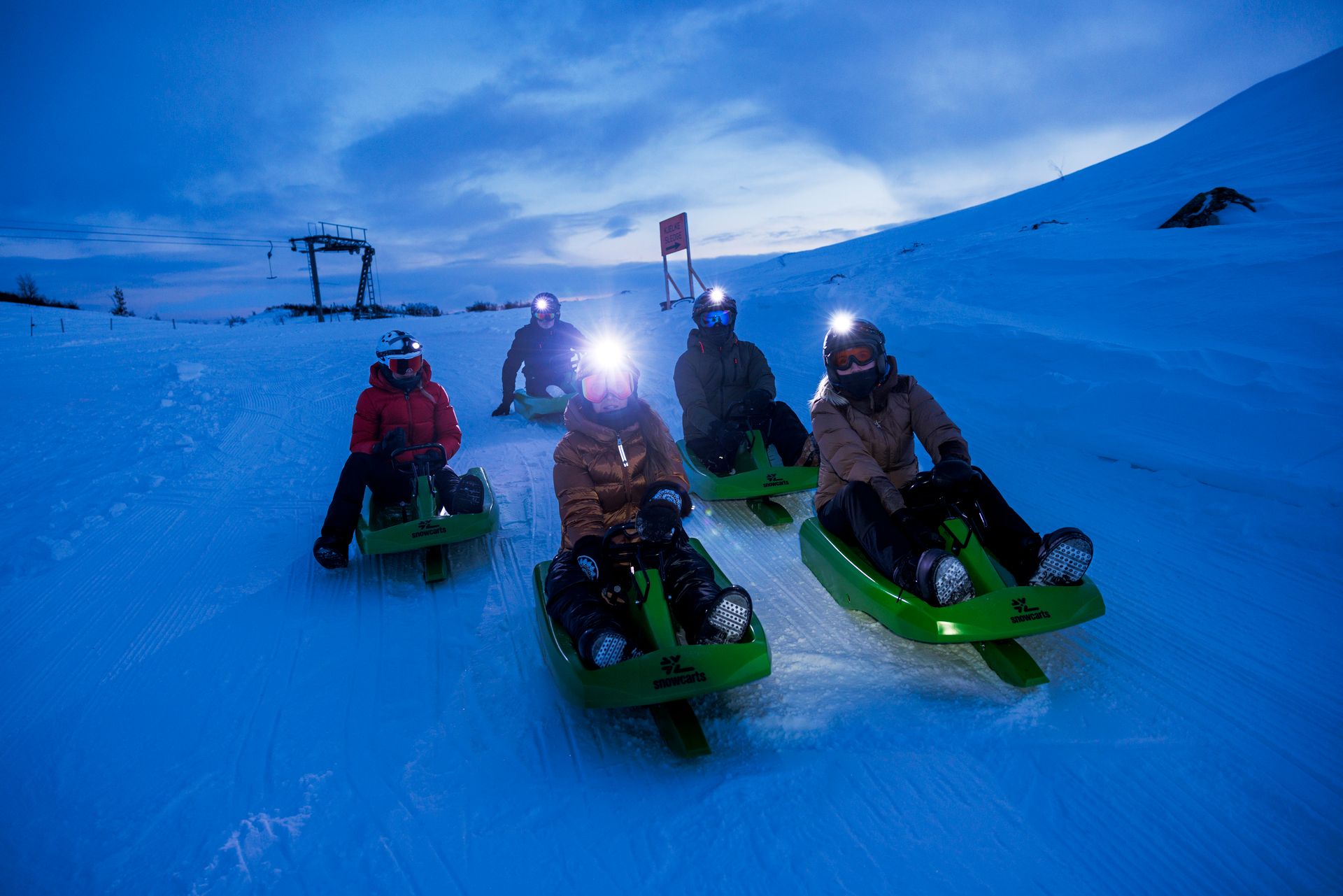 En gruppe på 5 sklir ned bakken med akebrett i mørket.