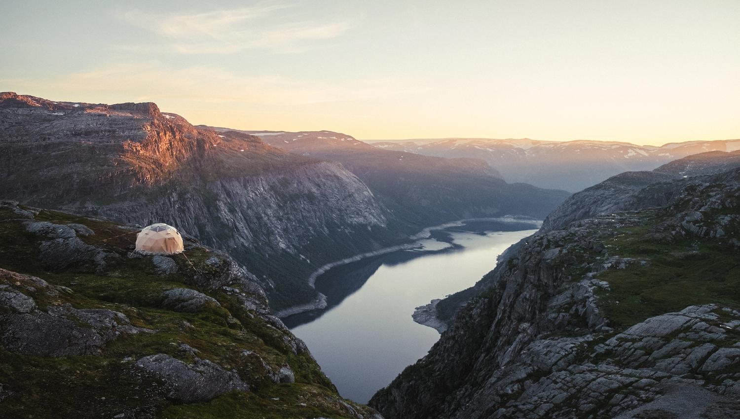 Et kuppelformet telt på fjellet med utsikt mot et fjellvann.