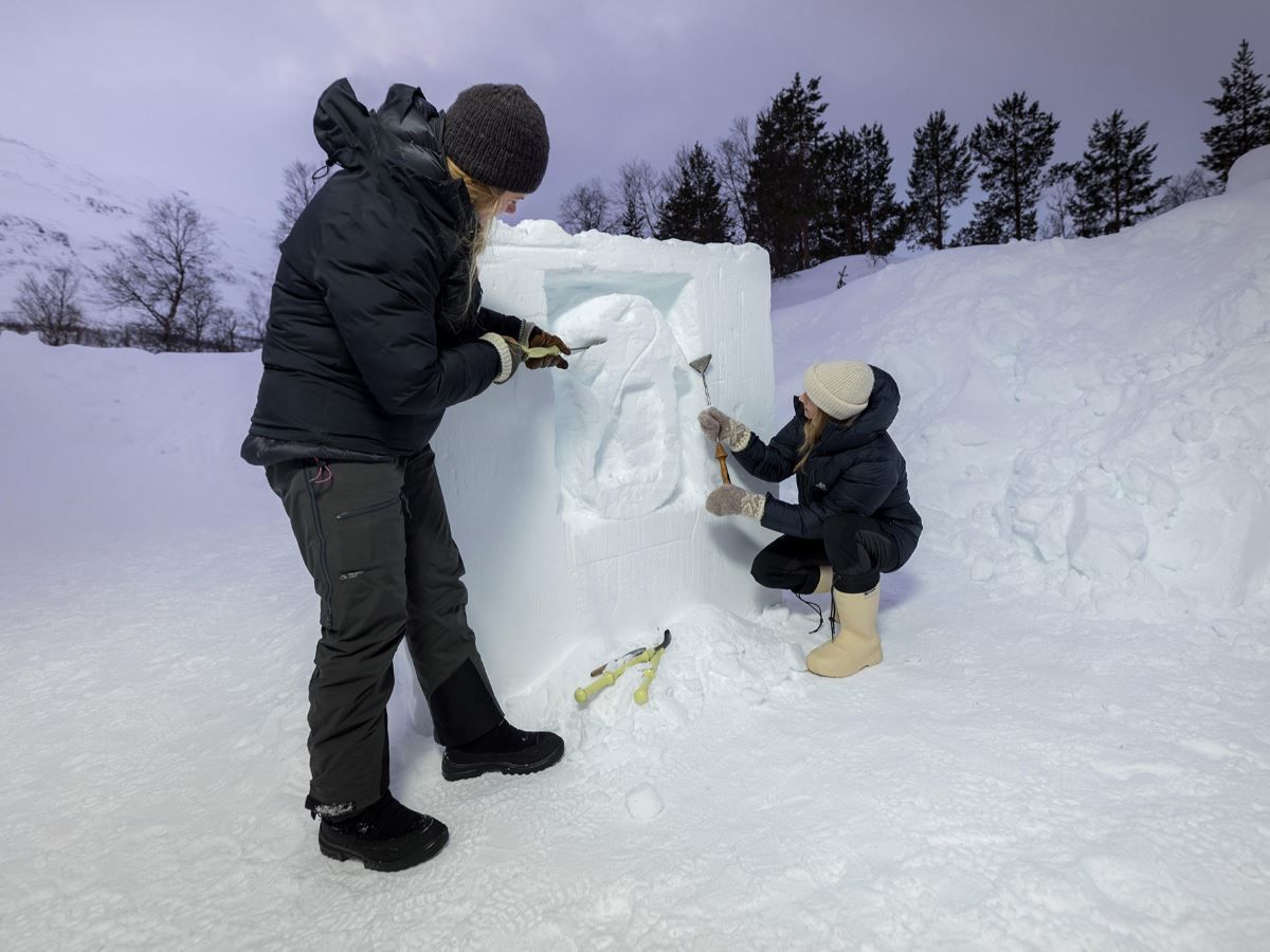 To gjester skulpturerer sin egen kunst i snøen med veiledning.