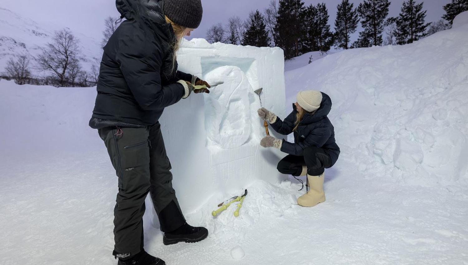 To gjester skulpturerer sin egen kunst i snøen med veiledning.