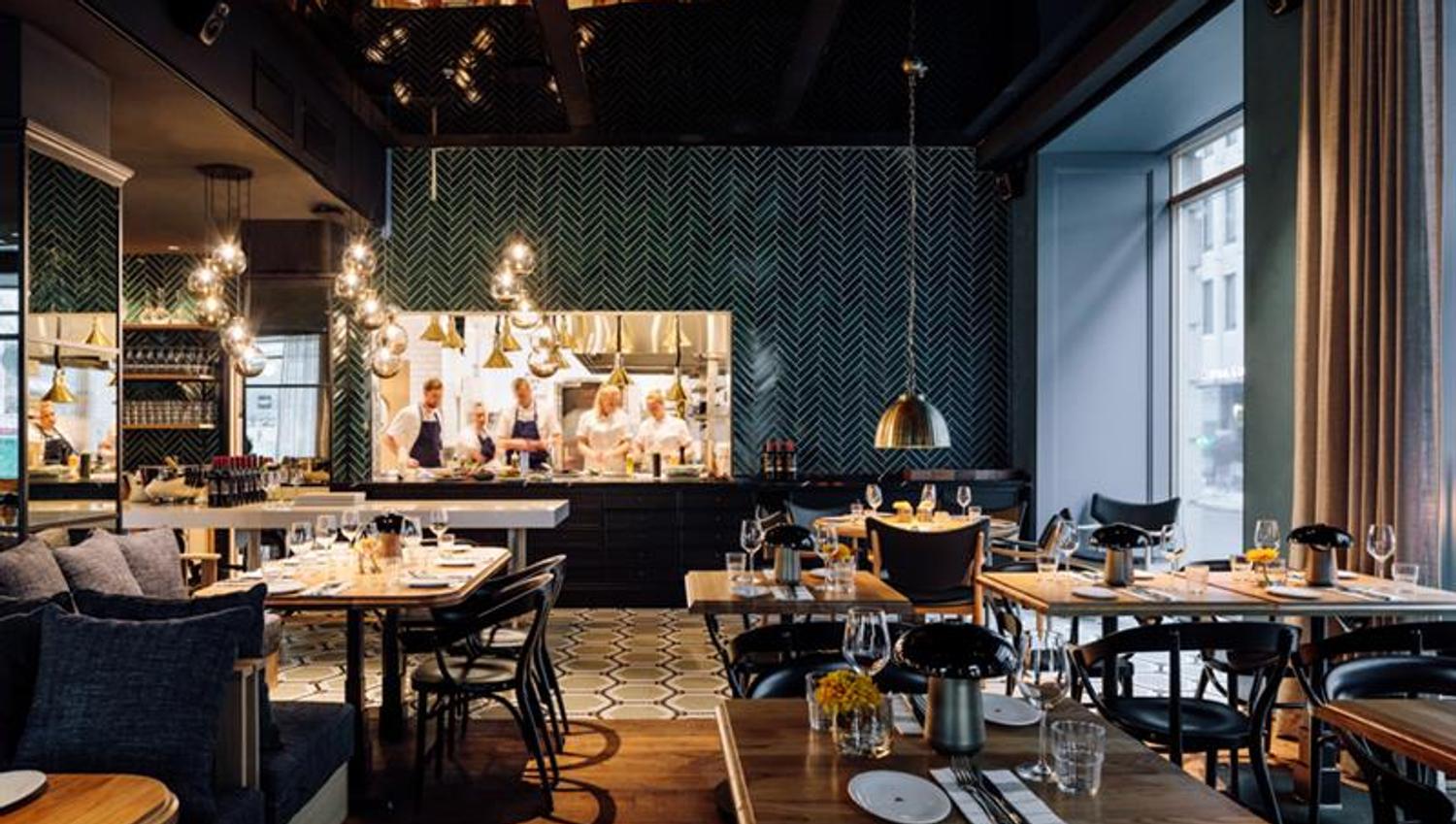 Restaurant Atlas - interior photo. Set tables with chairs, seating section, hanging ceiling lamps and the kitchen in the background.