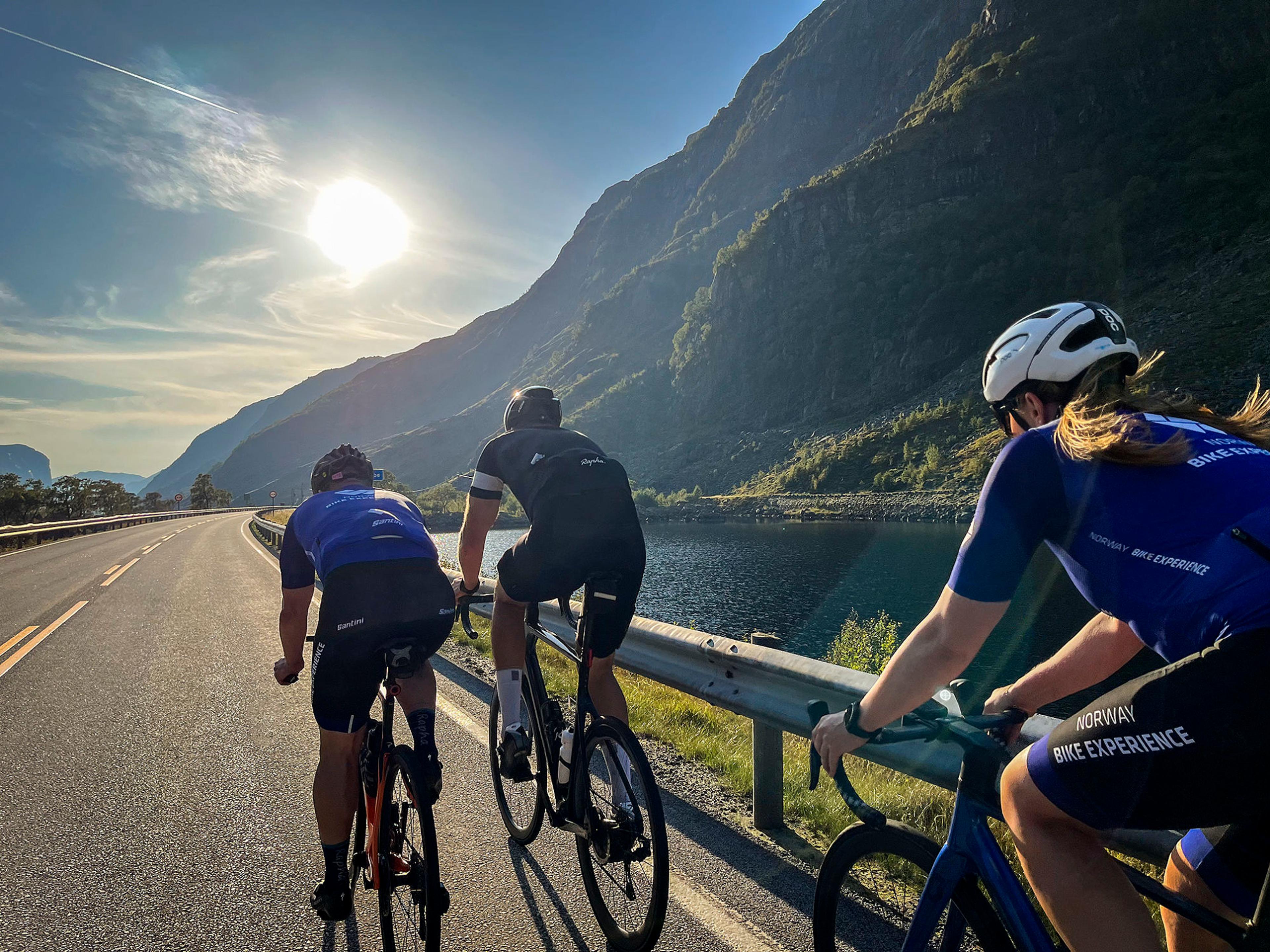 Tre syklister på tur med sol, fjell og vann