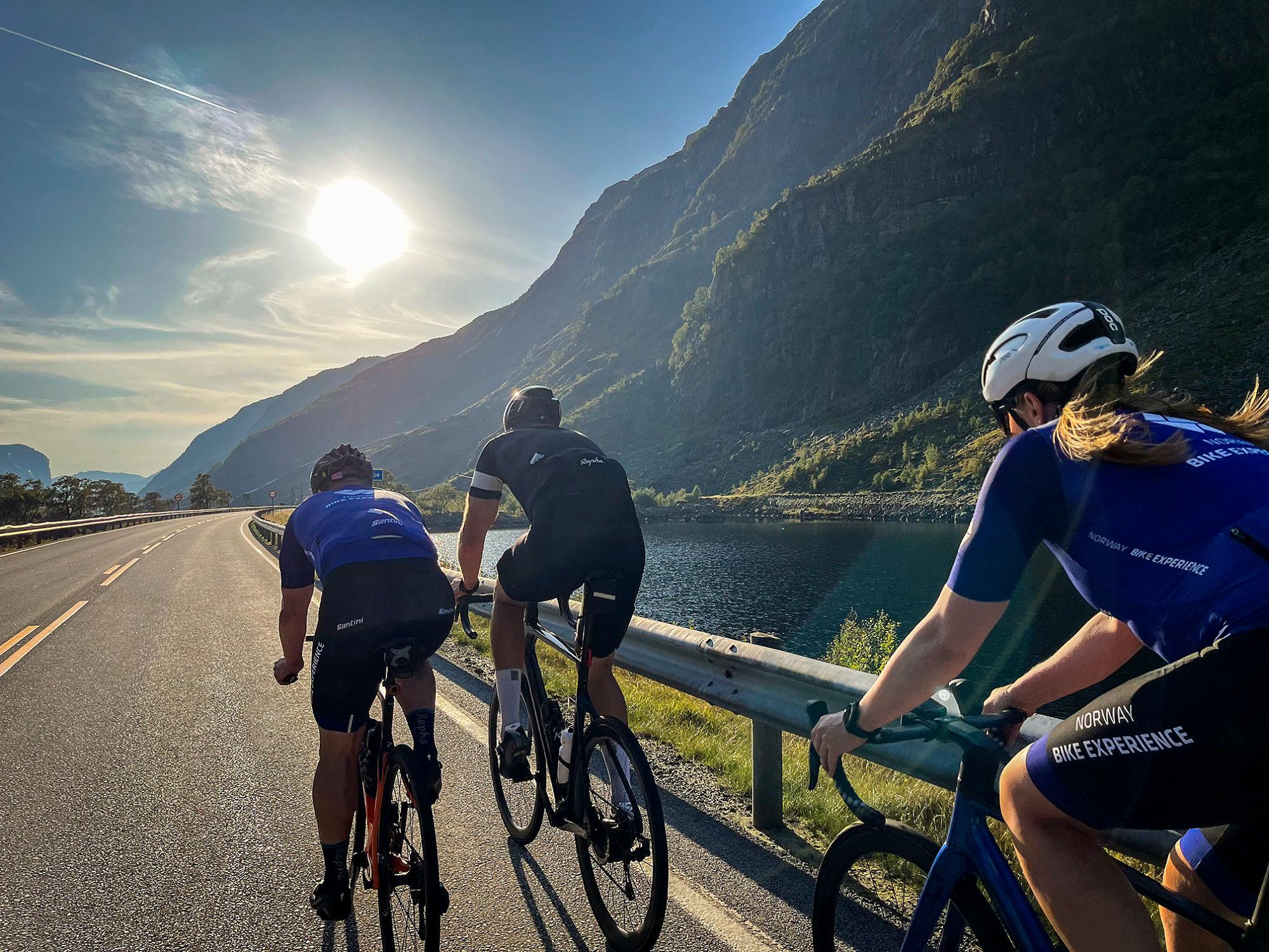 Tre syklister på tur med sol, fjell og vann