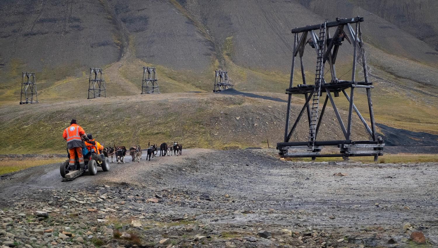 A dog team driving next to an old mining installation