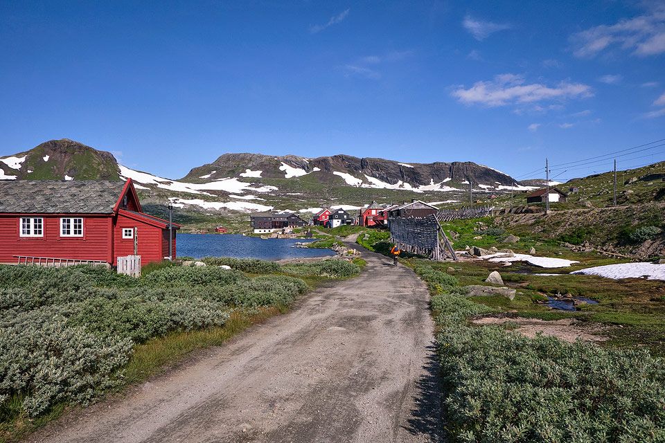 Utsikt mot Finse med raude fjellhytter og Rallarvegen under snødekte fjelltoppar.