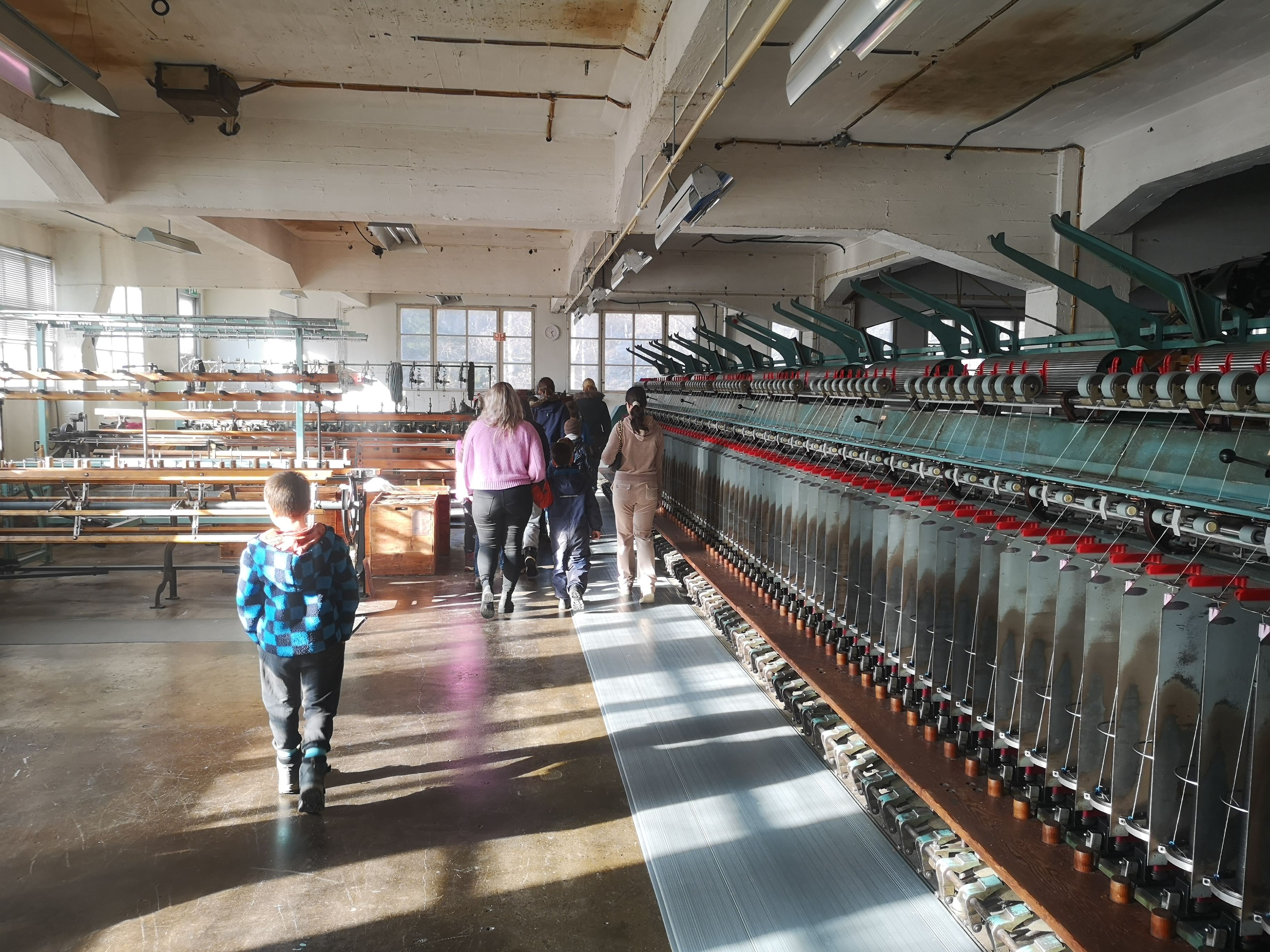 Exhibition inside the wool factory, a group is walking around and looking at the machines.
