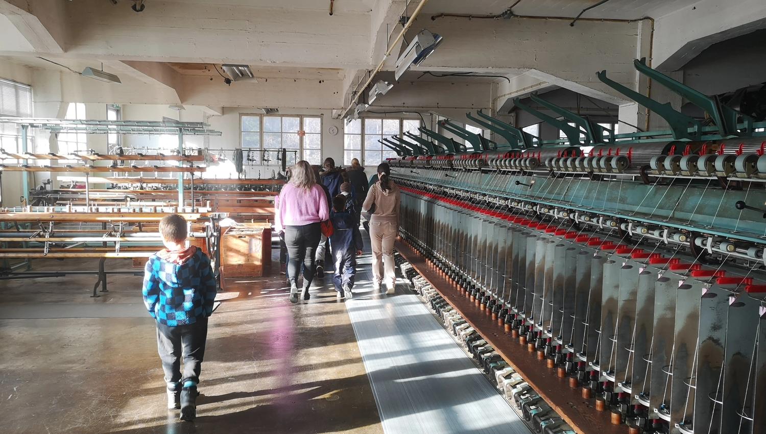 Exhibition inside the wool factory, a group is walking around and looking at the machines.