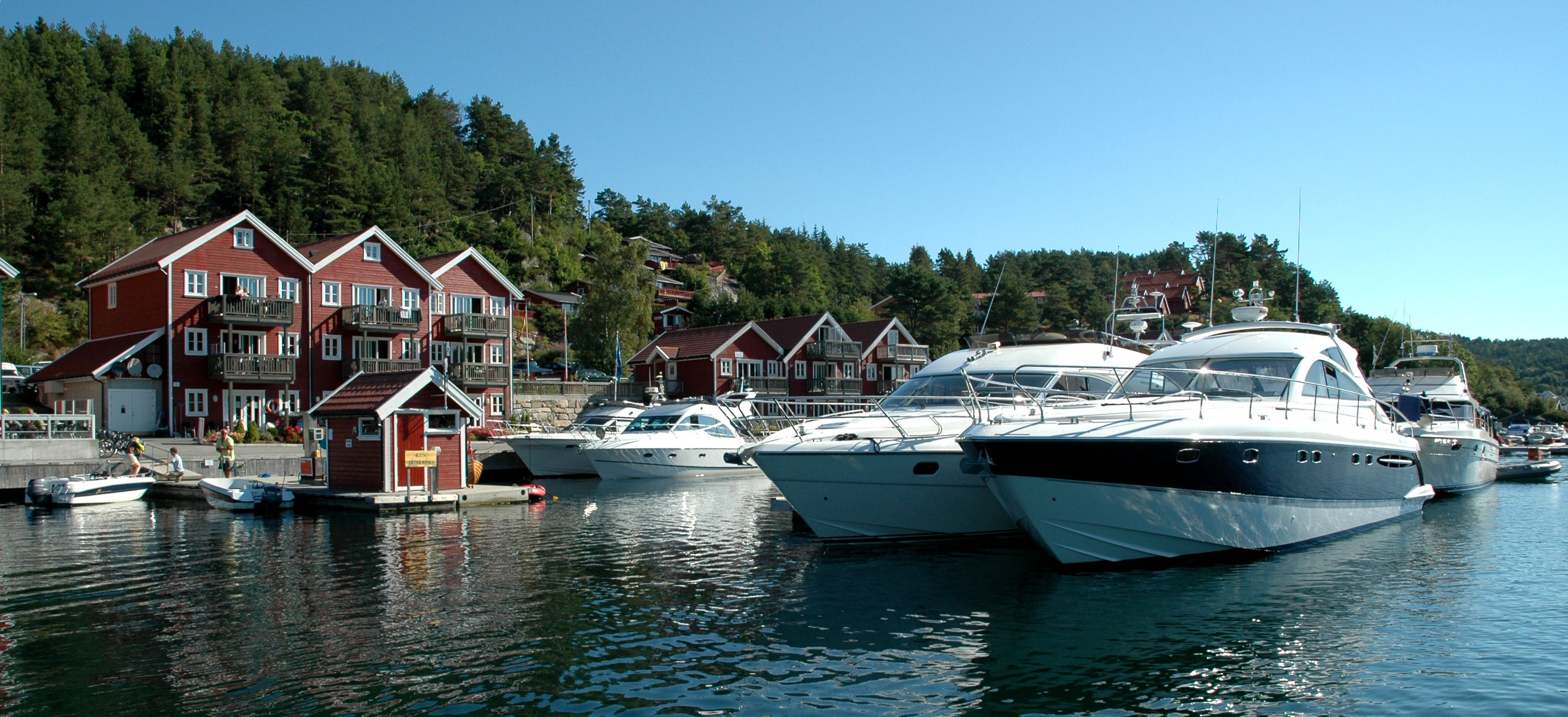 Three large boats are lined up in a row at the dock, with Tregde holiday homes in the background.

