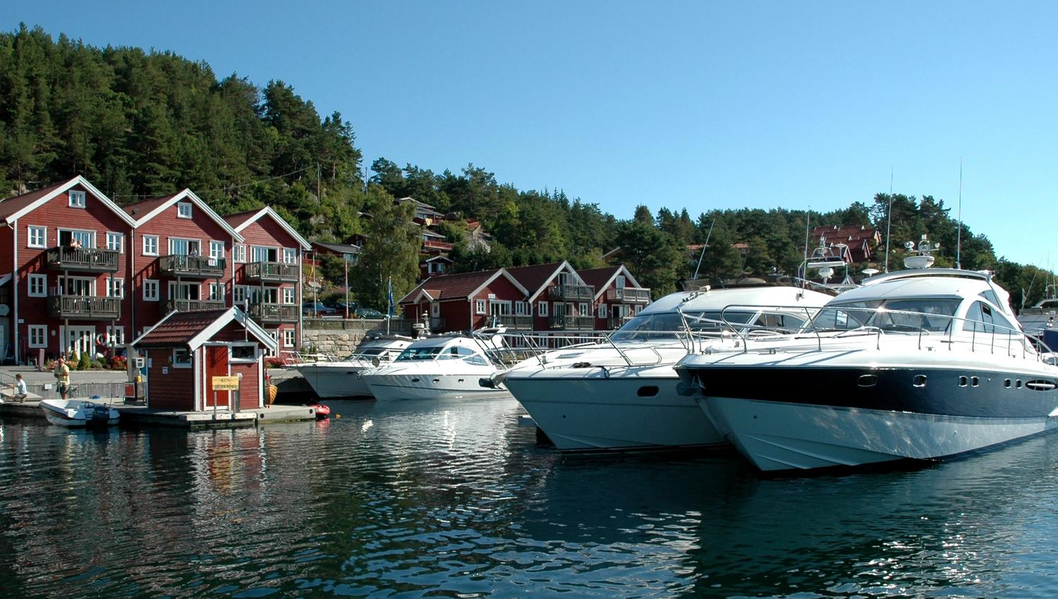 Three large boats are lined up in a row at the dock, with Tregde holiday homes in the background.