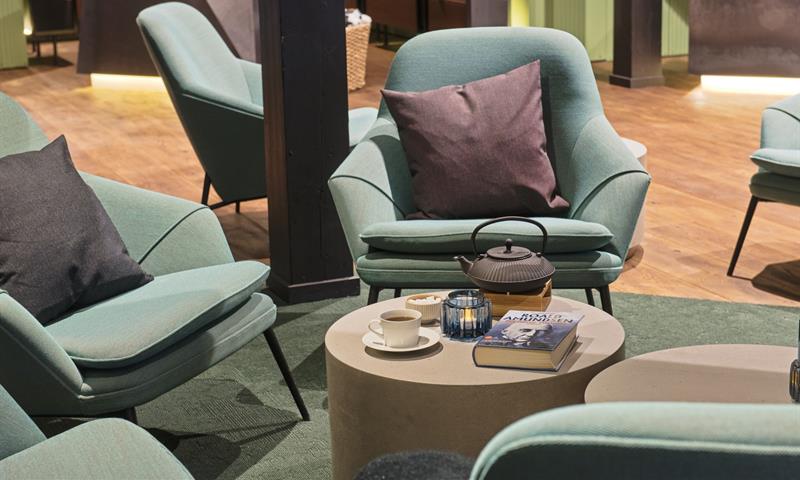 A small table with a coffee pot, a book and a coffee cup in the middle of a group of chairs in a hotel lobby