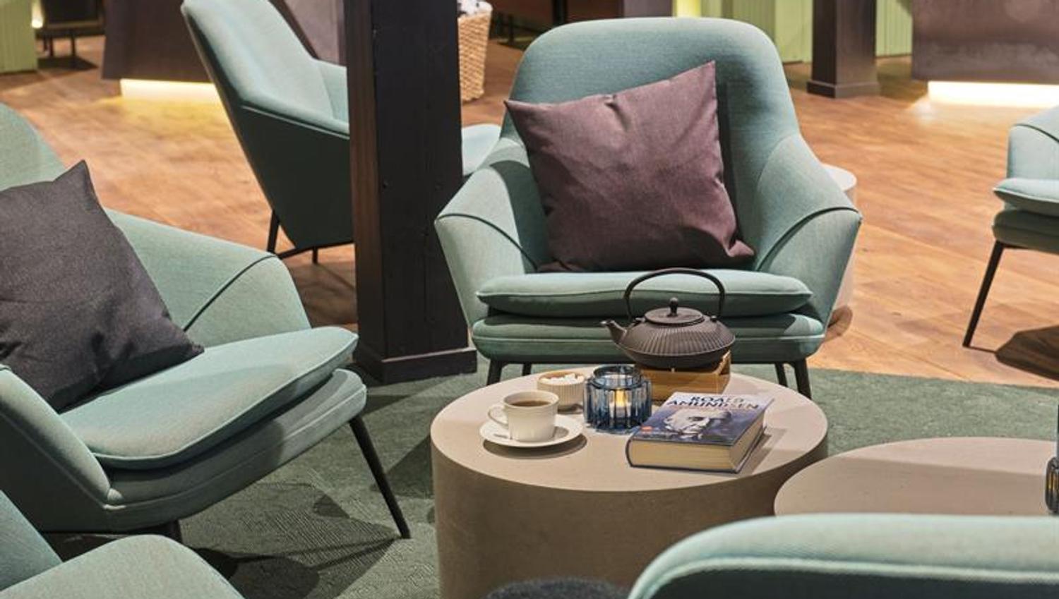 A small table with a coffee pot, a book and a coffee cup in the middle of a group of chairs in a hotel lobby