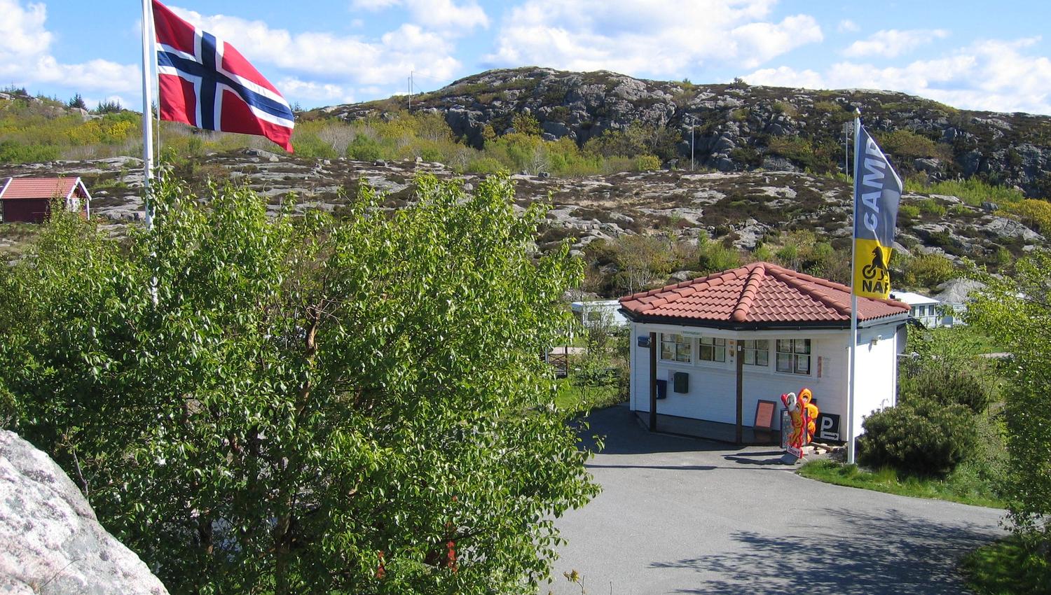 Resepsjonen og kiosken i samme hvite bygningen, norsk flagg på flaggstanga vedsiden av bygningen