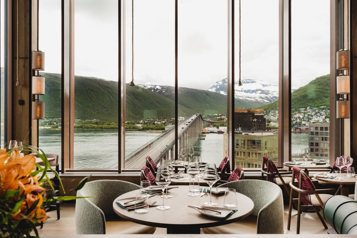 Restaurant with a view of a bridge, water, and mountains through large windows