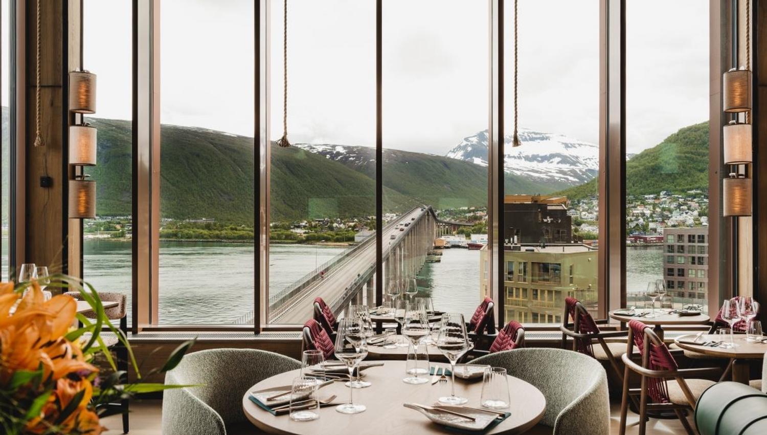 Restaurant with a view of a bridge, water, and mountains through large windows