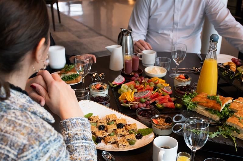 Bord dekket med ulike retter, drikke og kaffe mens flere personer sitter samlet rundt måltidet