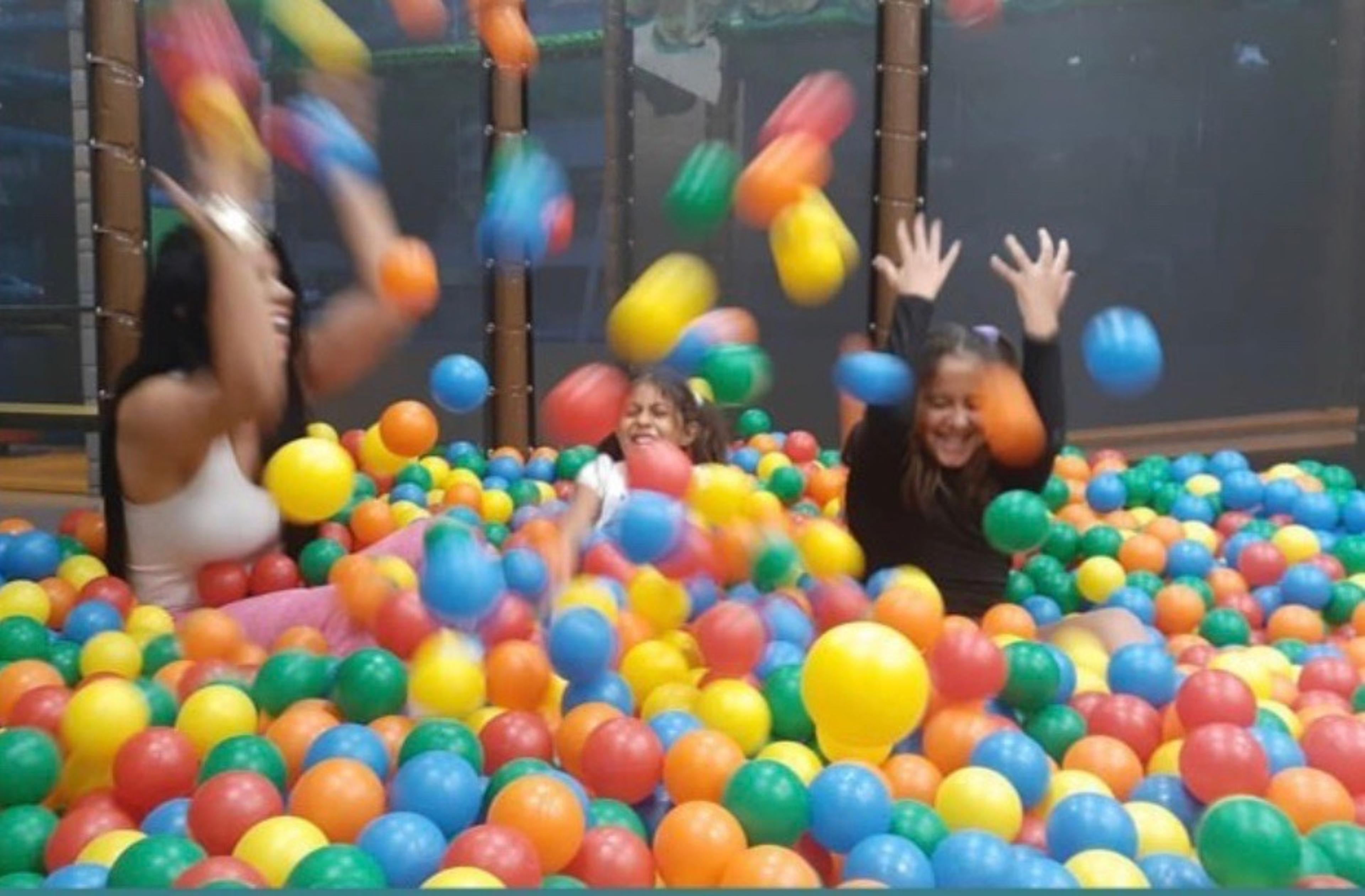 The ballroom, a room crammed full of colorful balls. 3 children are playing and throwing balls into the air.