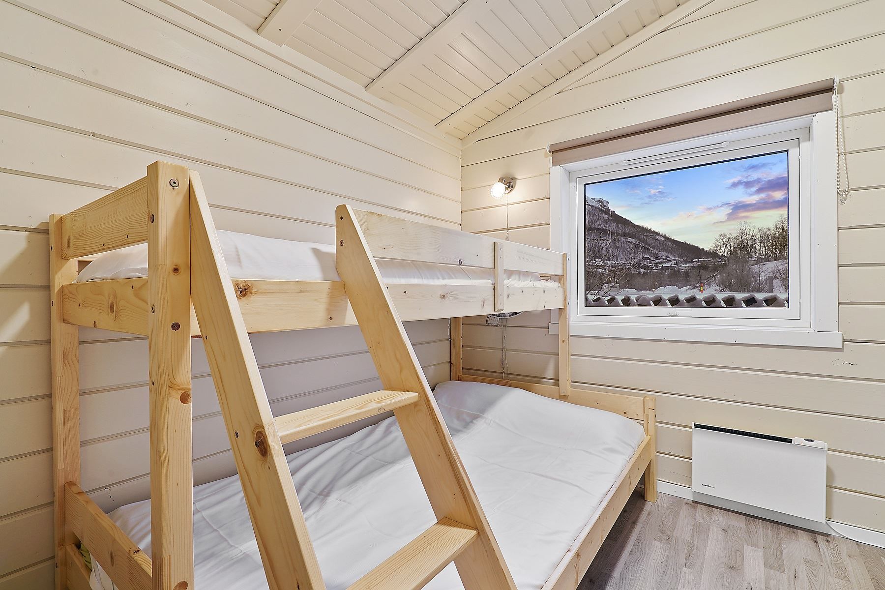 Small room with bunk bed and window with view of mountains and colourful sky