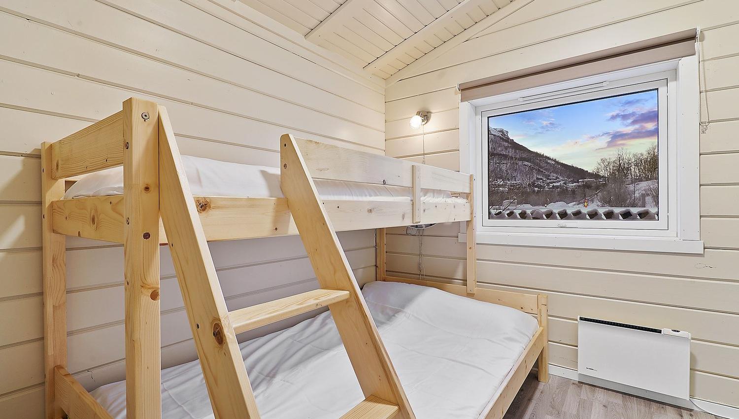 Small room with bunk bed and window with view of mountains and colourful sky
