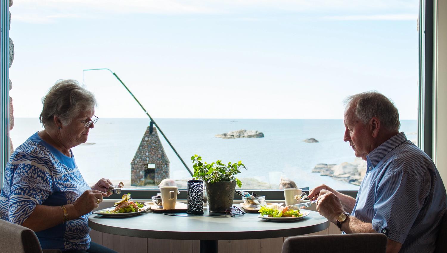 Two people eat food at Verdens Ende Spiseriet with a view to the tilting lighthouse