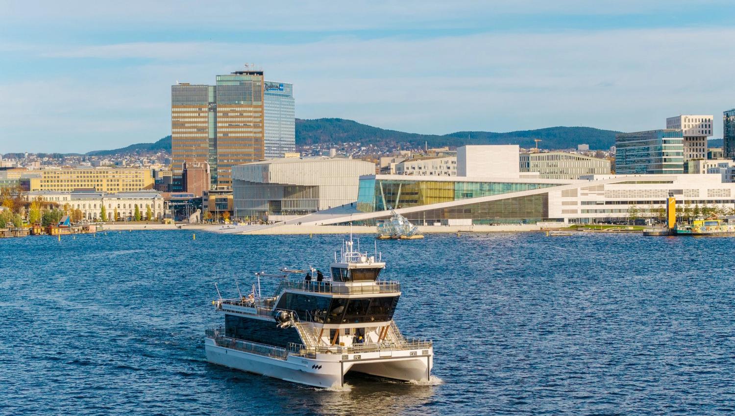 Drone image of the boat in the fjord with the city in the background.