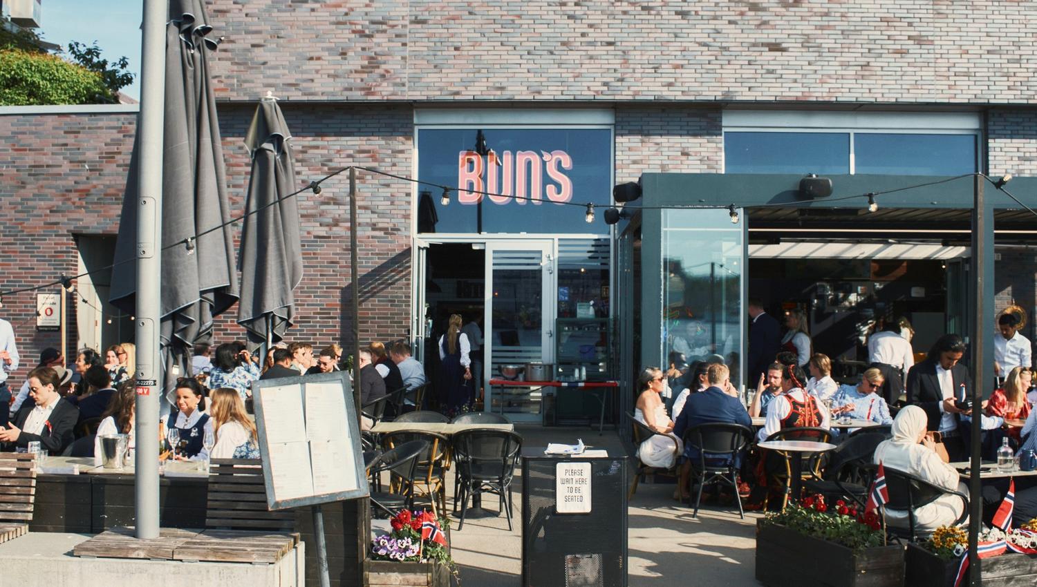 Uteservering med gjester som koser seg i solen foran restauranten.