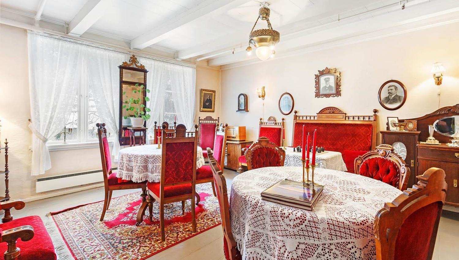 Historic dining room with antique furniture, red velvet chairs, and lace tablecloths at Jaunsen Gjestgjevarstad in Granvin.