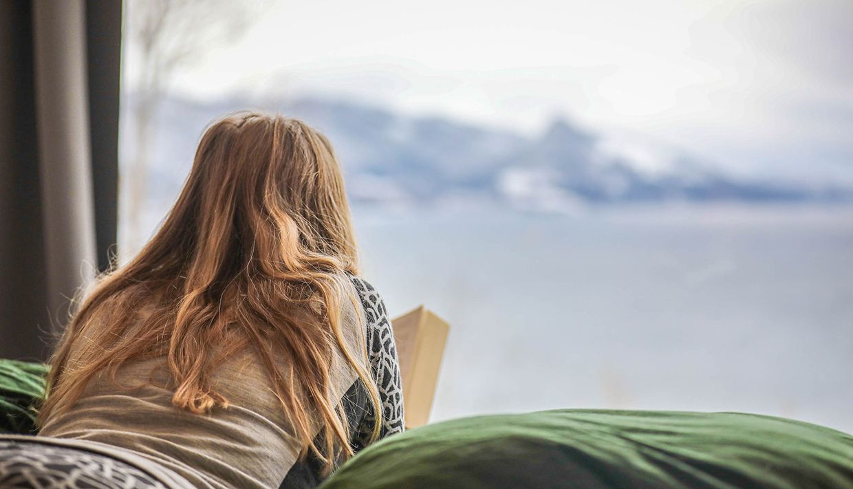 Close-up of a guest enjoying the fjord view from bed in the cabin near Hardangerfjord.