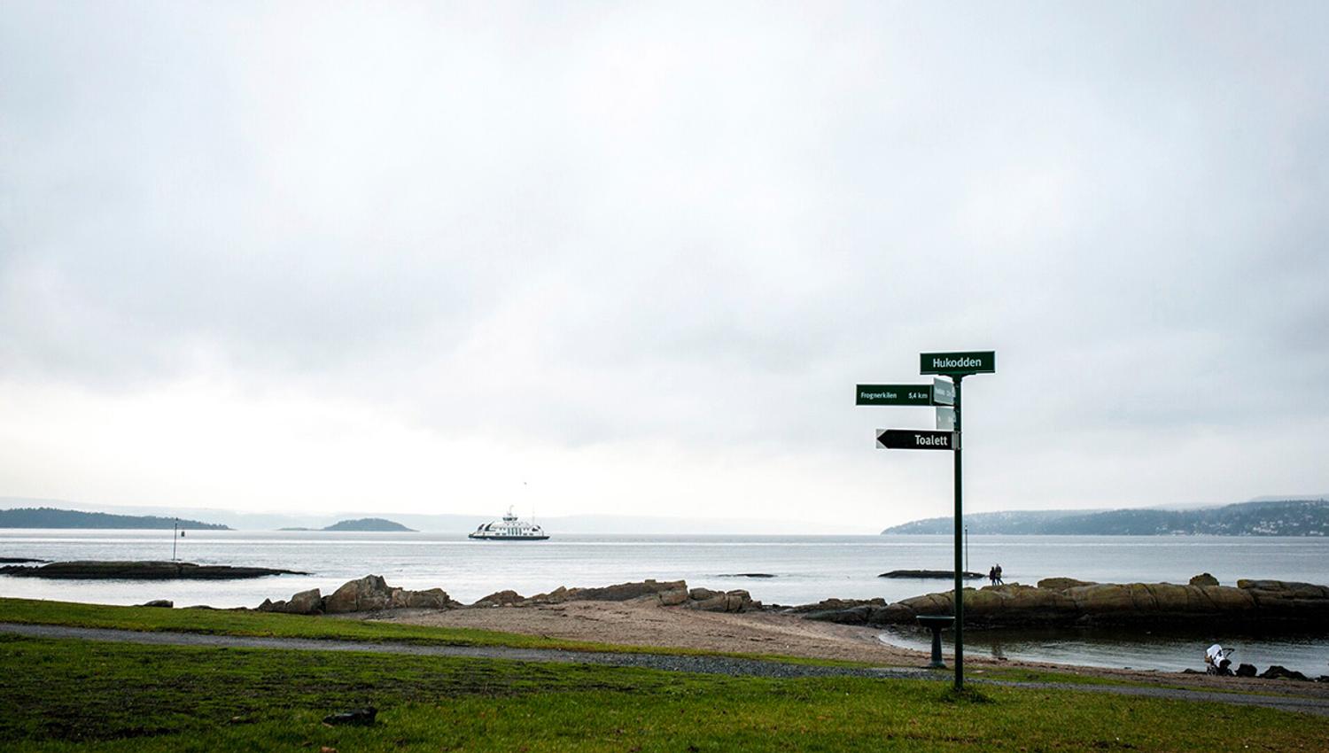 strand på bygdøy med skilt og en av øyfergene i bakgrunnen