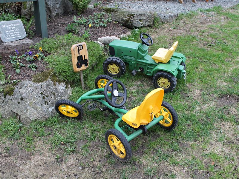 To grønne lekebiler, en traktor og en gocart lignende bil plassert ved lekeparkeingsplass.