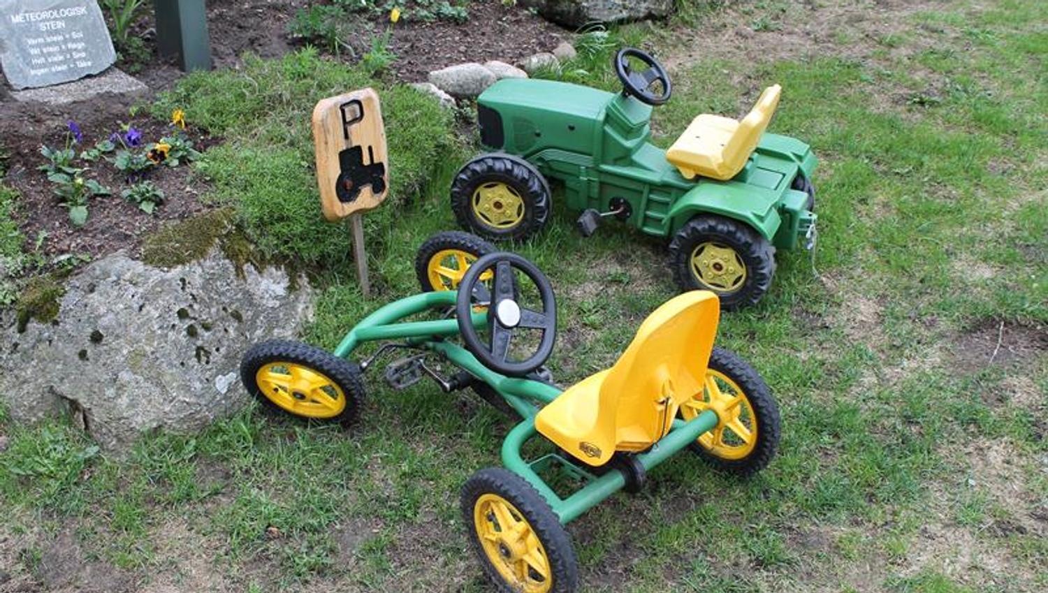 To grønne lekebiler, en traktor og en gocart lignende bil plassert ved lekeparkeingsplass.