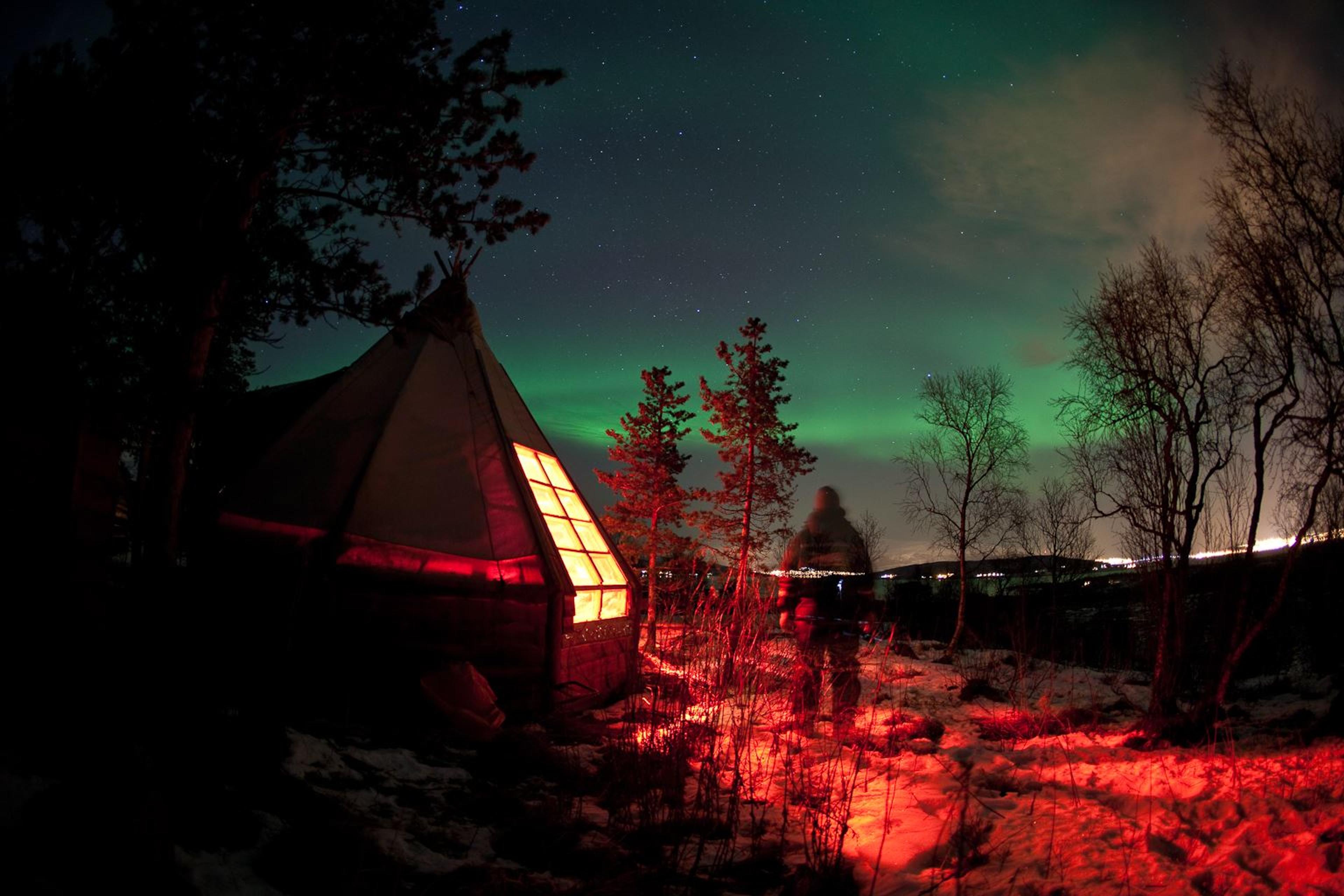 Guest outside one of the huts enjoying the northern lights in the sky
