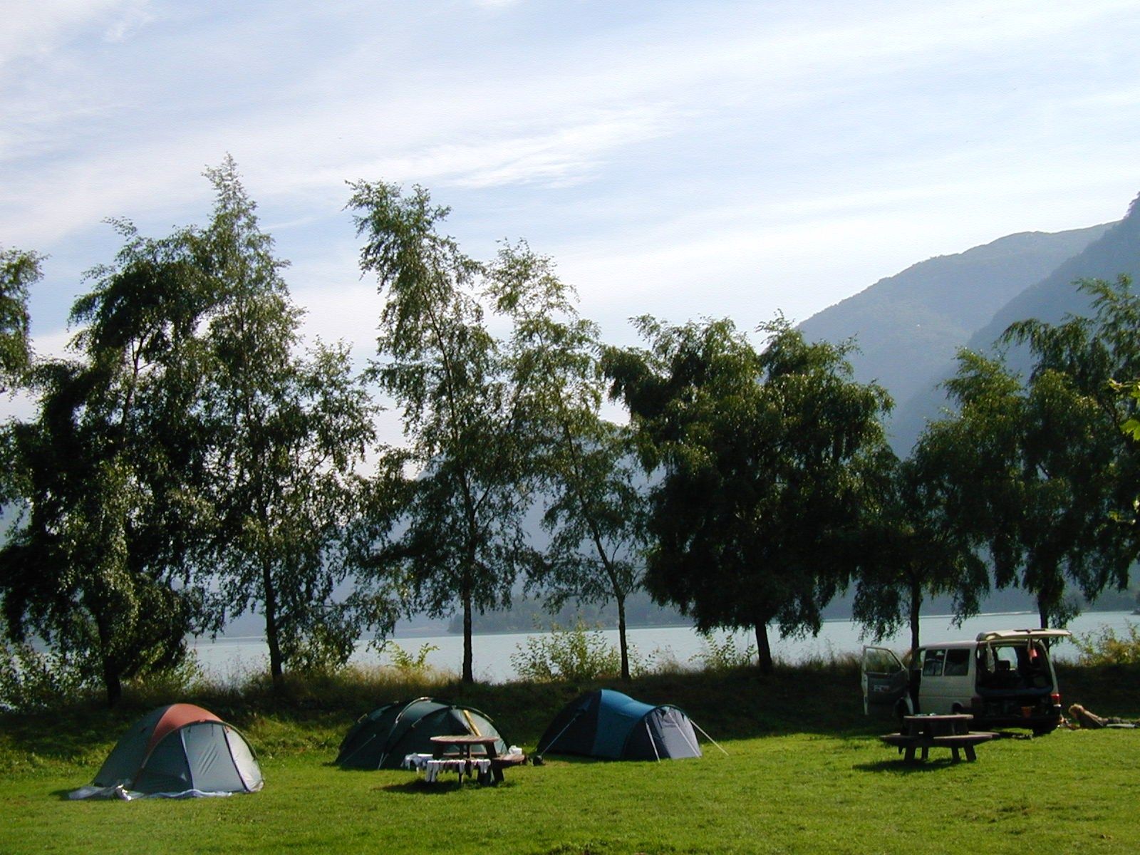 Teltområde på grasplen ved fjorden omgitt av tre og fjell.