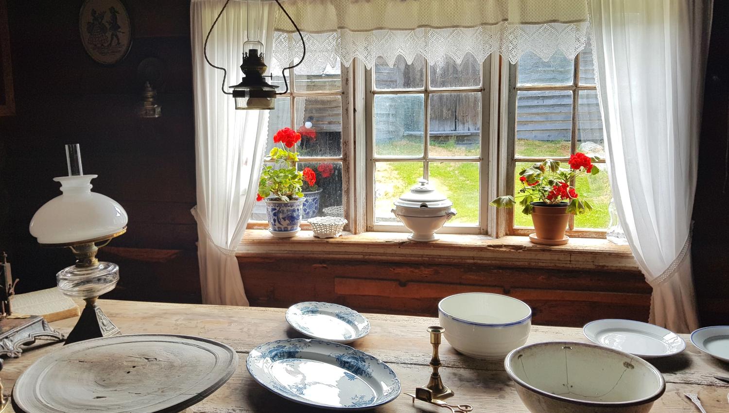 Eit dekka bord ved eit vindu med blomar og kvite blondegardiner