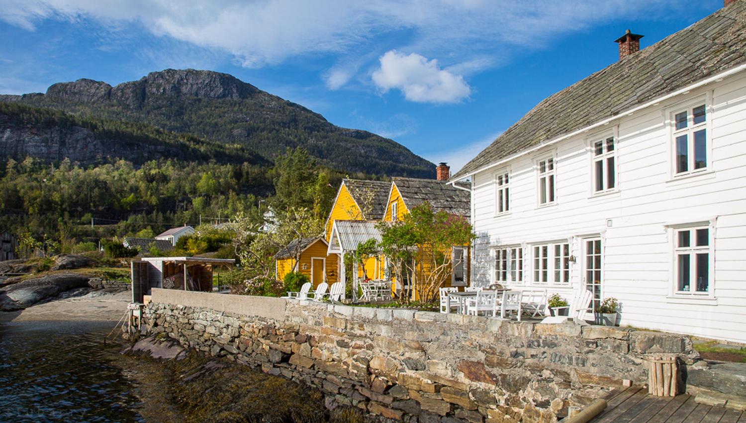 Kramsjø Gjestgiveri i Hardanger – sjarmerande kvite og gule hus ved fjorden, omgitt av vakker natur og majestetiske fjell.
