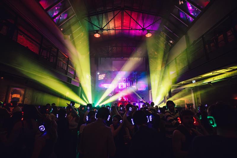 Silent disco-arrangement: Dansegulv fullt av folk med hodetelefoner på og neonlys