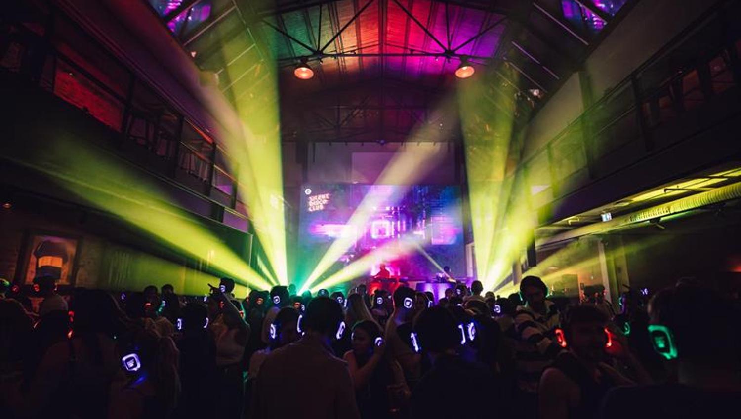 Silent disco-arrangement: Dansegulv fullt av folk med hodetelefoner på og neonlys