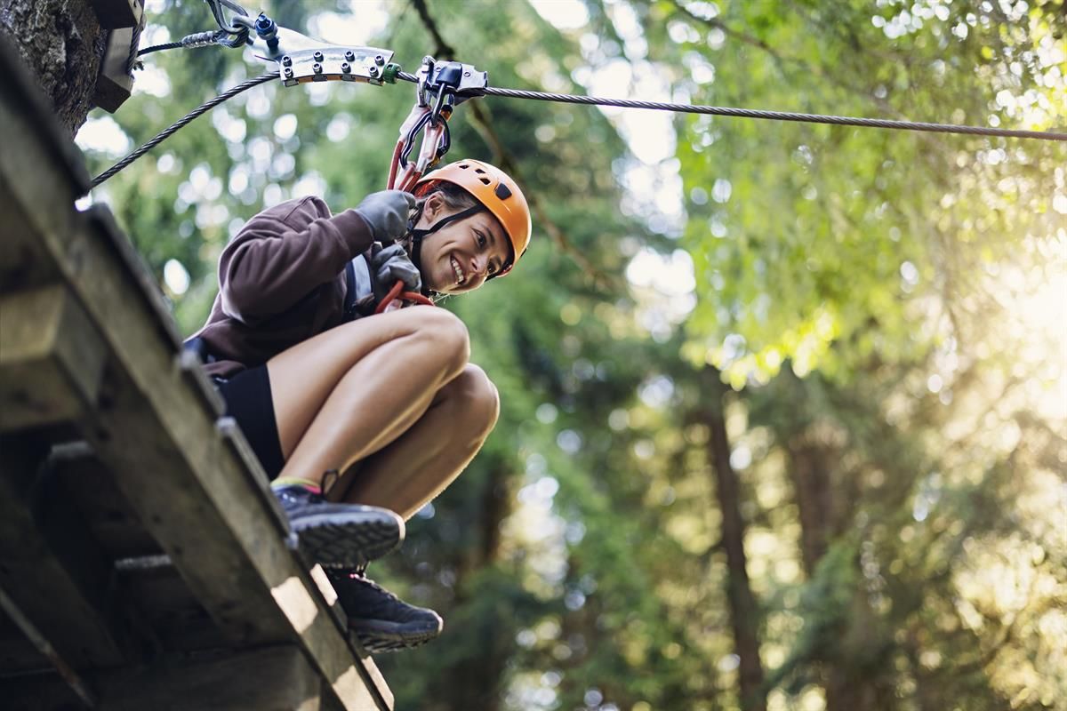 A person riding a zipline through the forest with sunlight in the background.