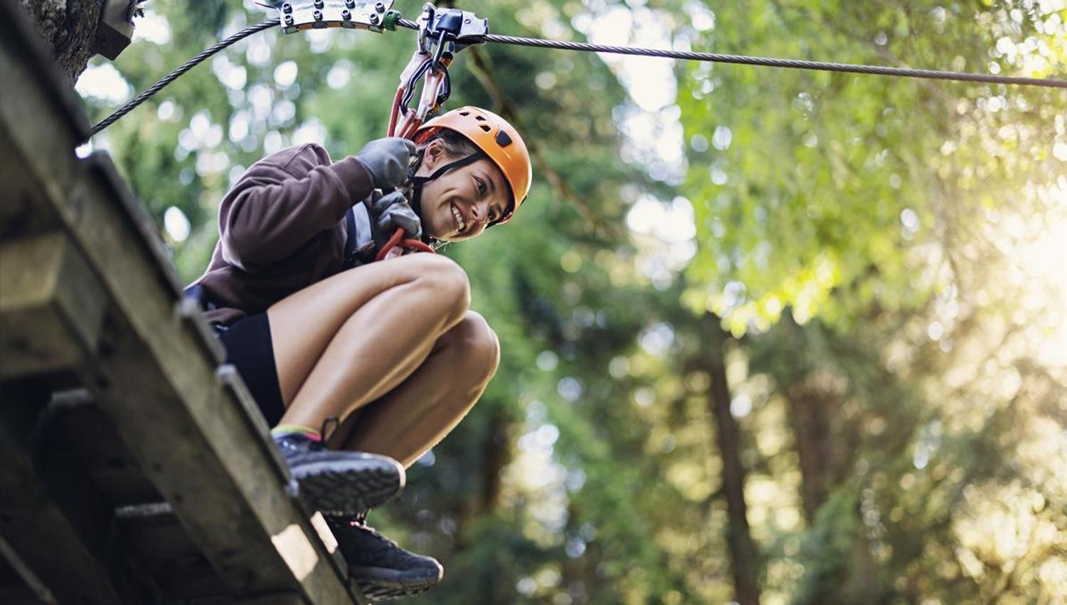 A person riding a zipline through the forest with sunlight in the background.