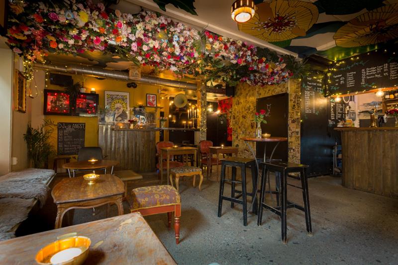 Interior of bar area with various tables and chairs in different sizes. Flower arrangements hanging from the ceiling.